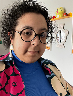 A smiling Afro-Mexican genderqueer person with round glasses, earrings and black curly hair.