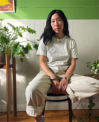 An Asian American woman with long hair sitting in a chair against a green and white wall.